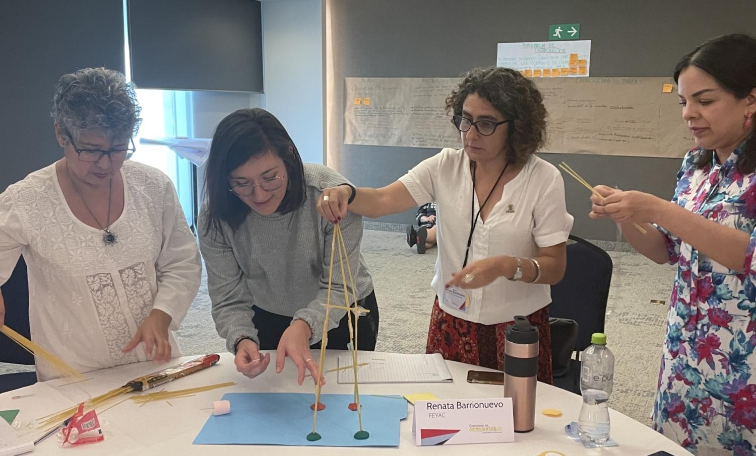 Group of four women building something out of spaghetti.  