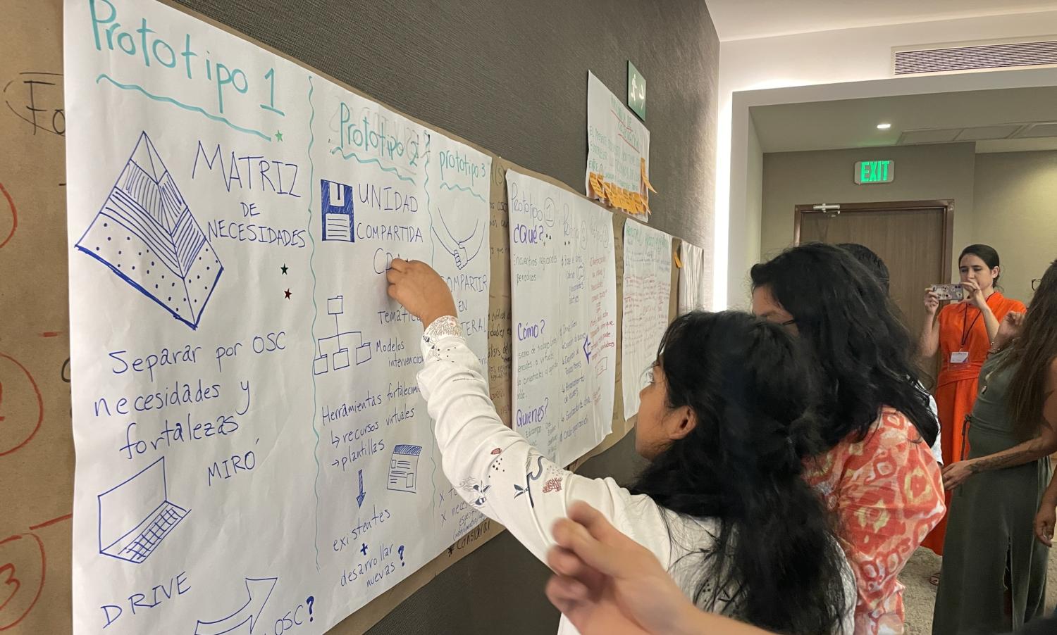 Two women are writing on large sheets of paper that mention prototyping.