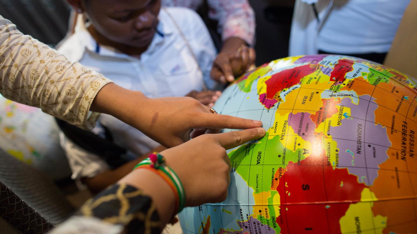 A young boy explores and points to places on a globe with others.